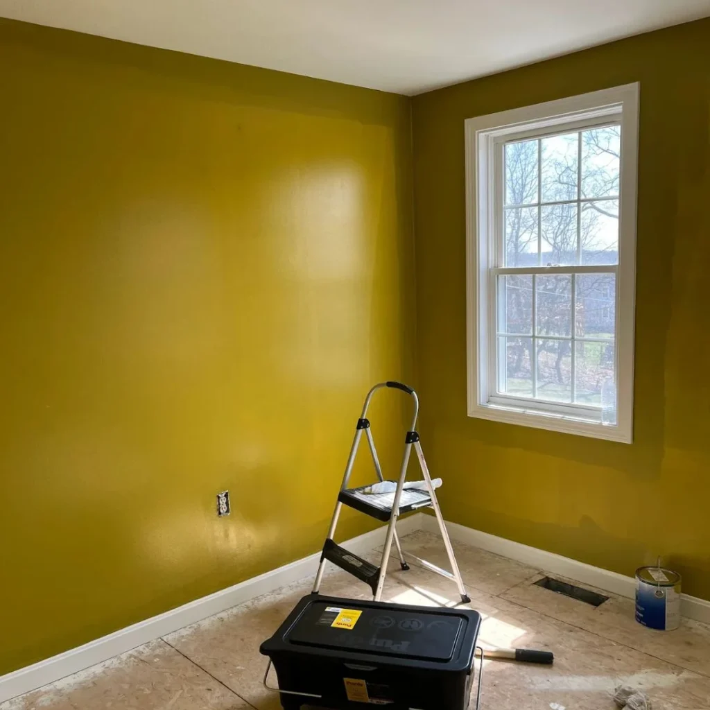 Interior painting project in a bedroom with freshly painted yellow walls, a step ladder, and painting supplies on the floor.