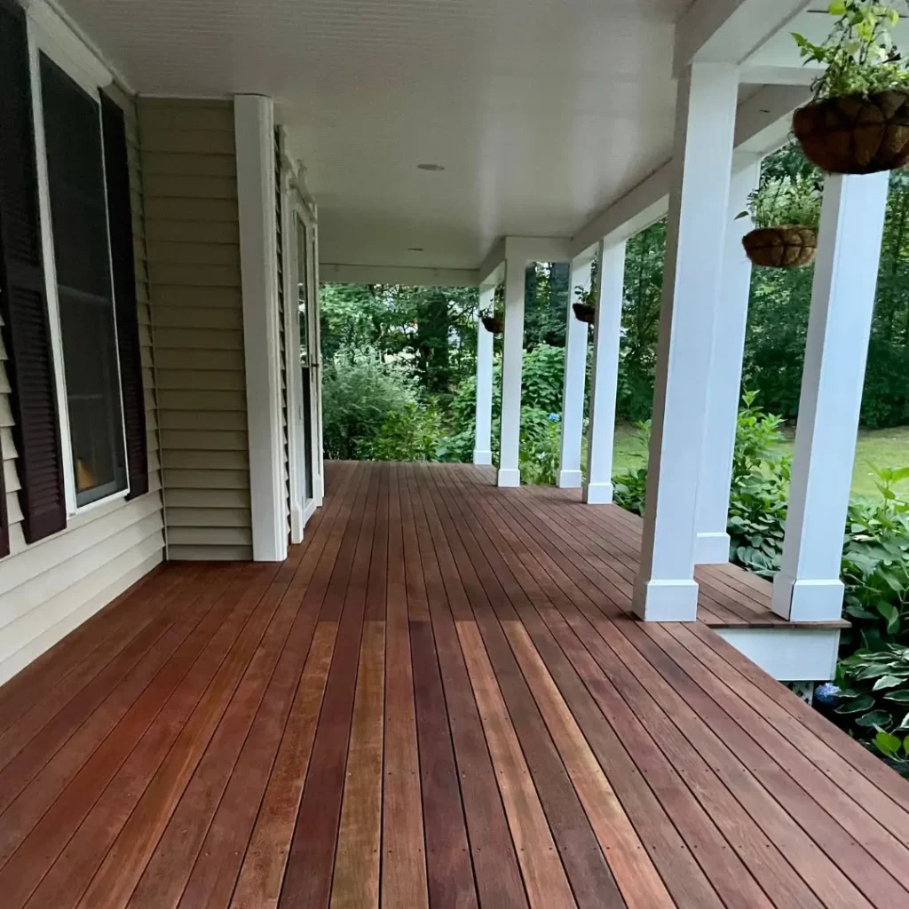 Deck stained in rich brown tones, showcasing a well-maintained wooden surface, surrounded by white columns and greenery, emphasizing exterior painting and staining services by Handymasters Painting Co.