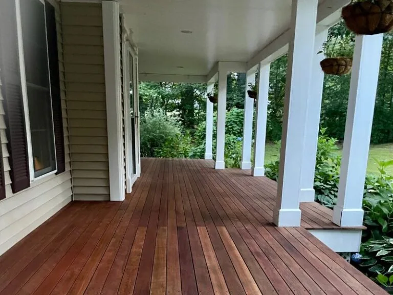 Stained wooden porch with white pillars and lush greenery, showcasing quality craftsmanship by Handymasters Painting Co. in Durham, NH.